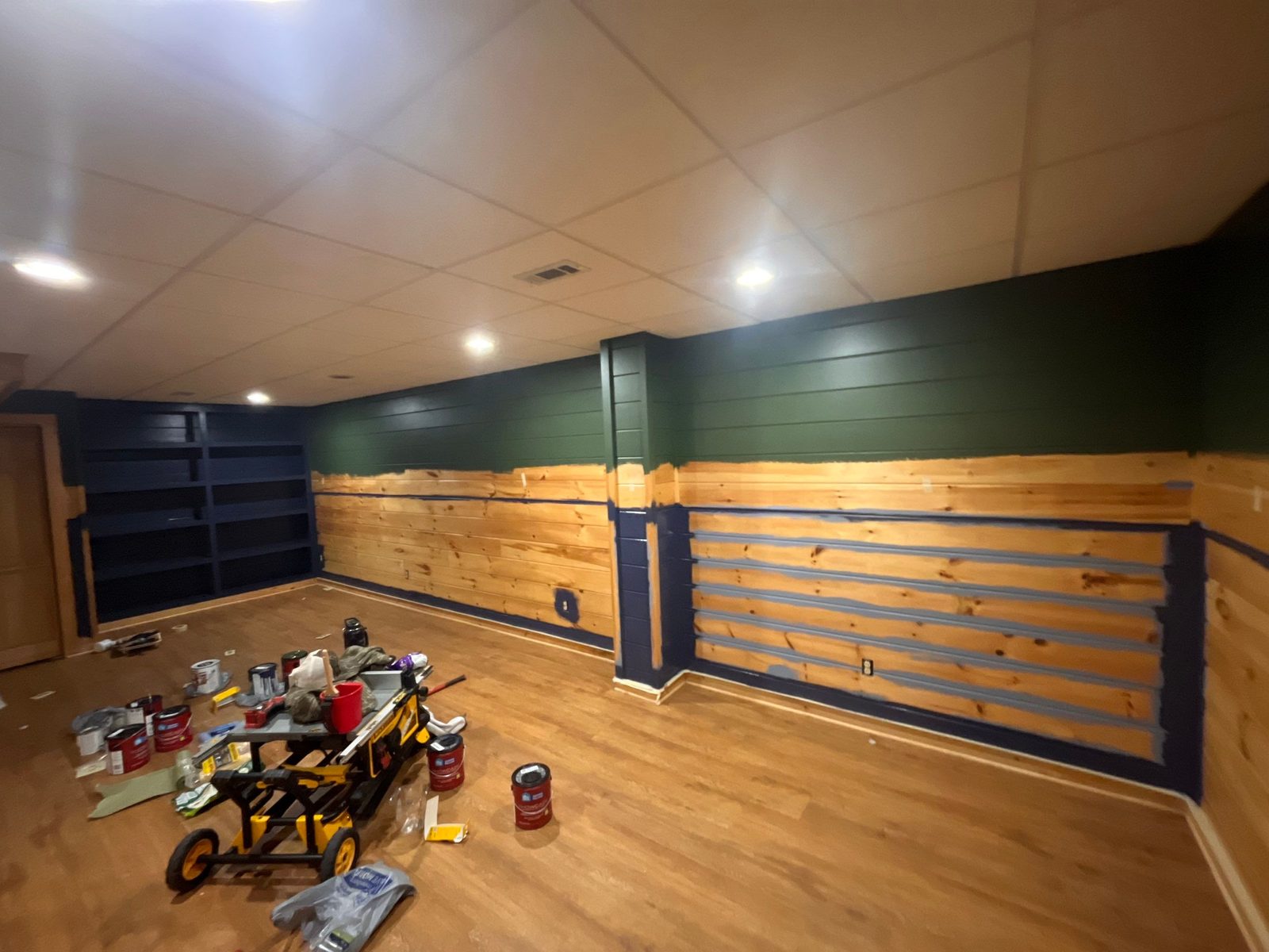 Basement shiplap mid-paint in Blue Ridge, GA, navy brushed into the seams of raw pine below green upper walls