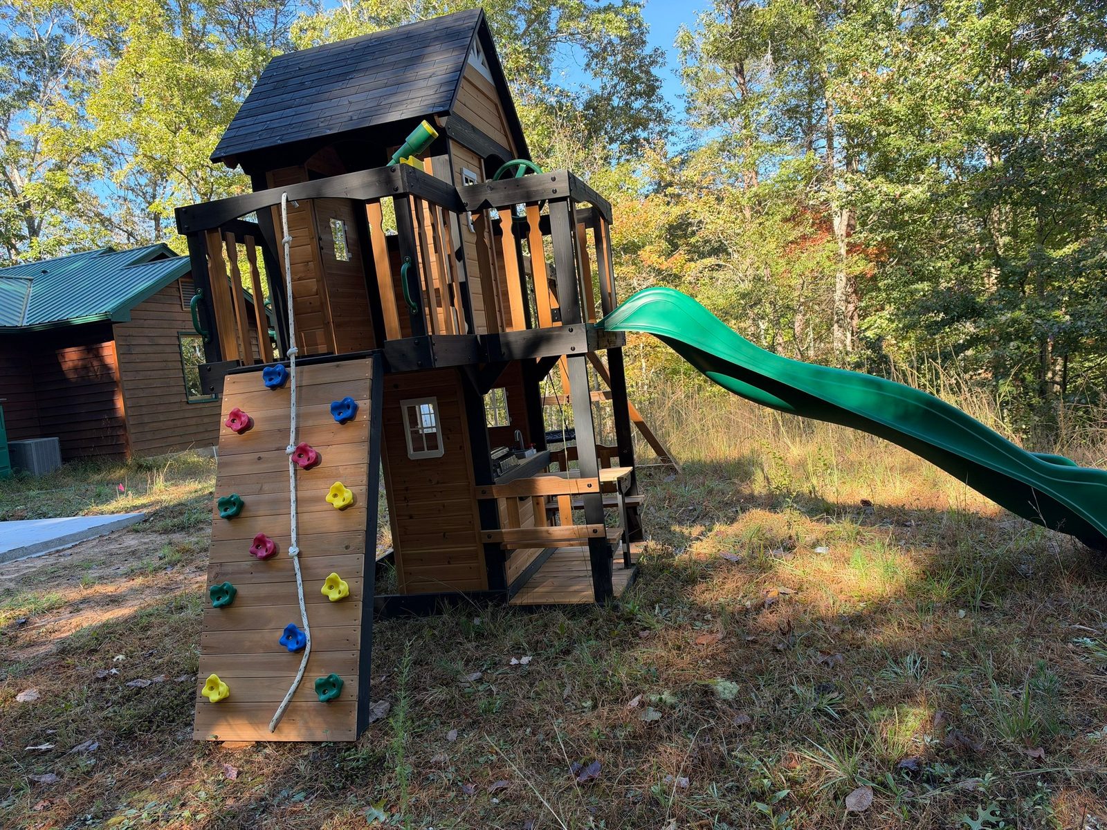 Wooden playset assembled at a Blue Ridge, GA cabin with a climbing wall, green slide and clubhouse