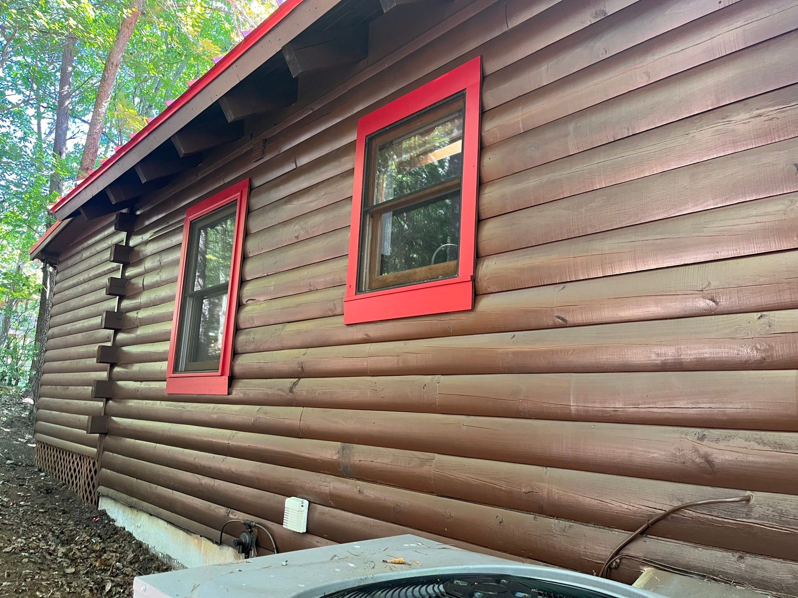 Stained log side wall with two red-trimmed windows on a Cherry Log cabin
