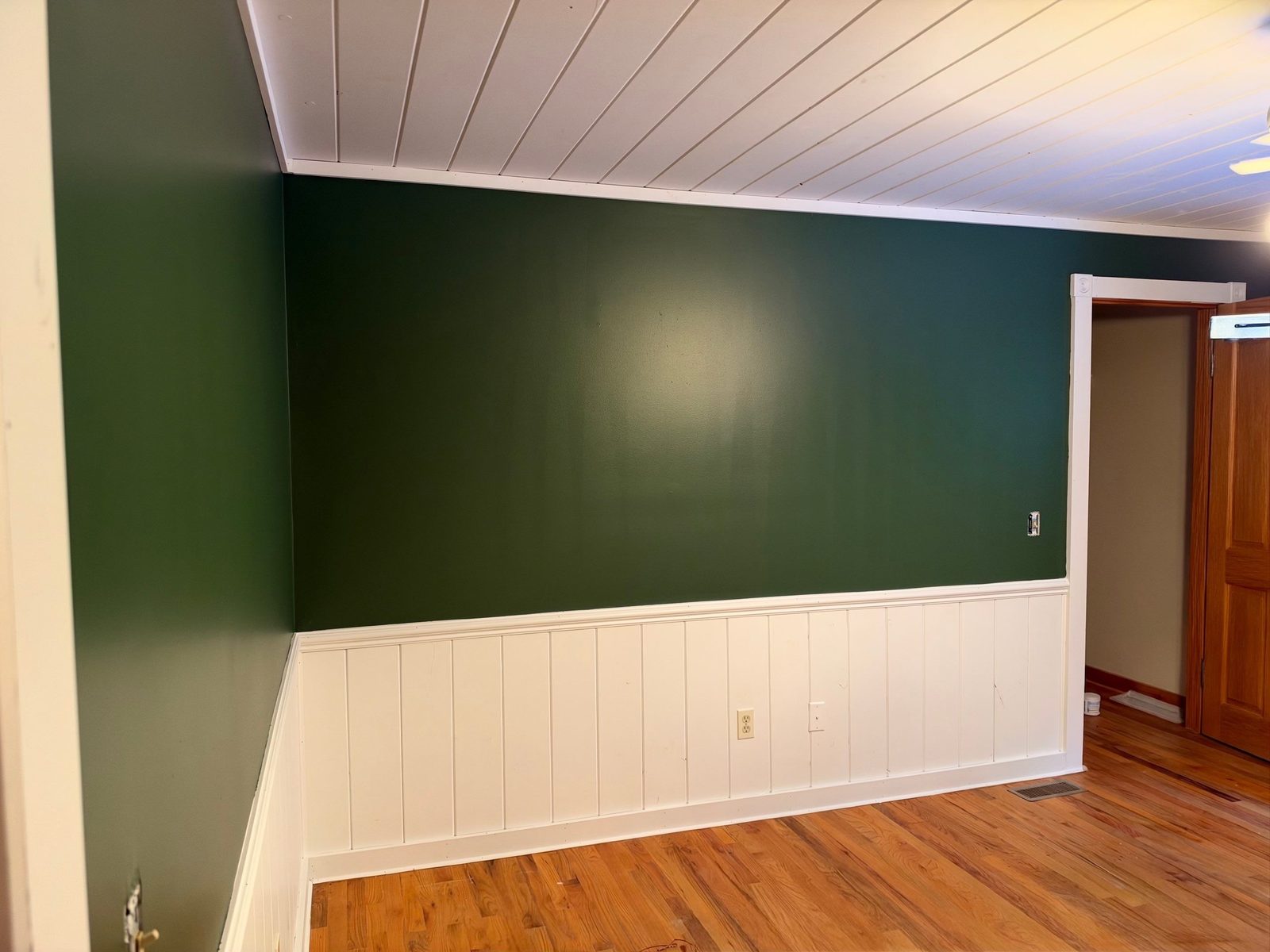 Dark green accent wall above white wainscot under a white plank ceiling in a Blue Ridge cabin