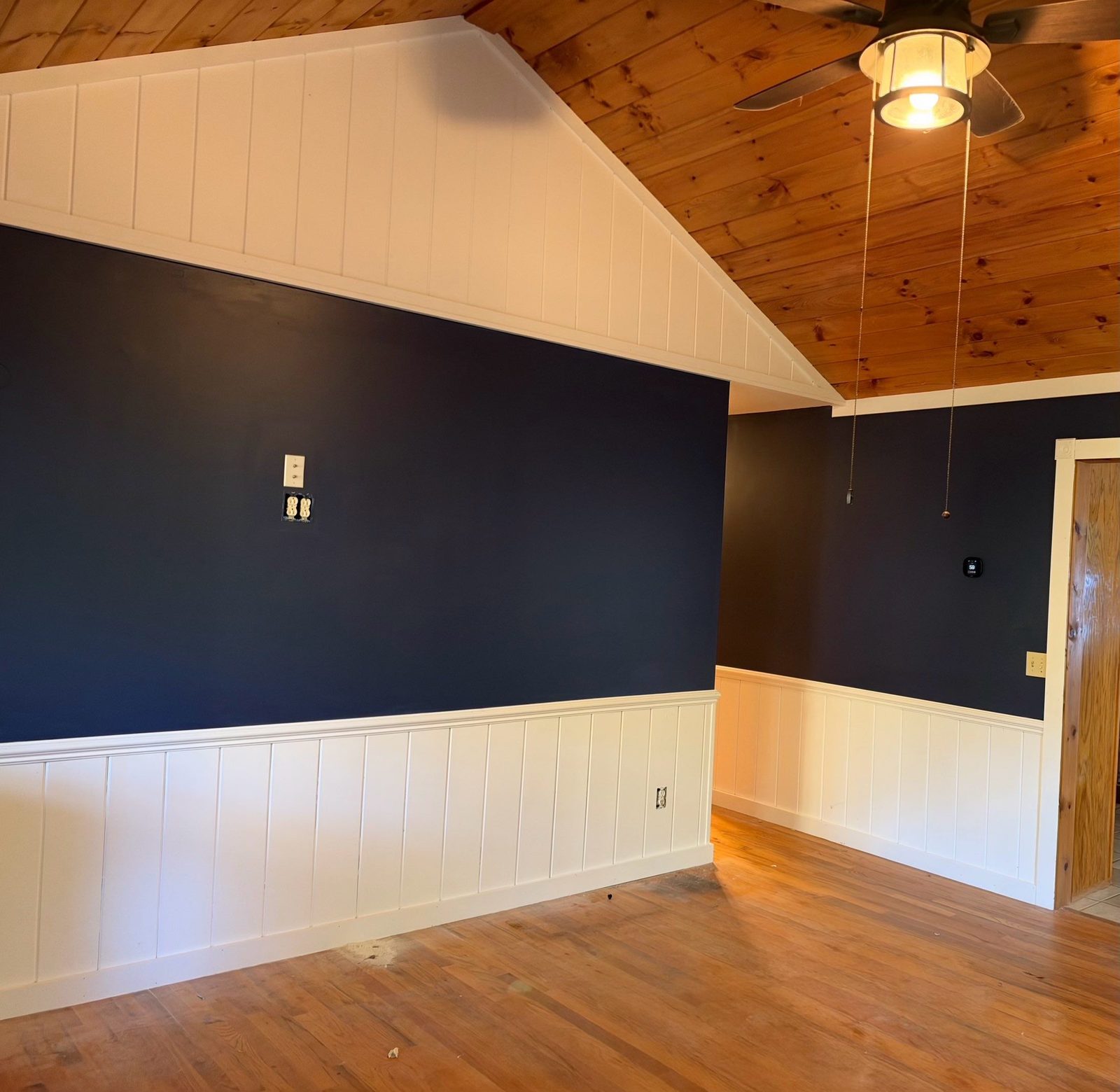 Navy walls over white vertical paneling in a Blue Ridge cabin bedroom with a pine ceiling and ceiling fan