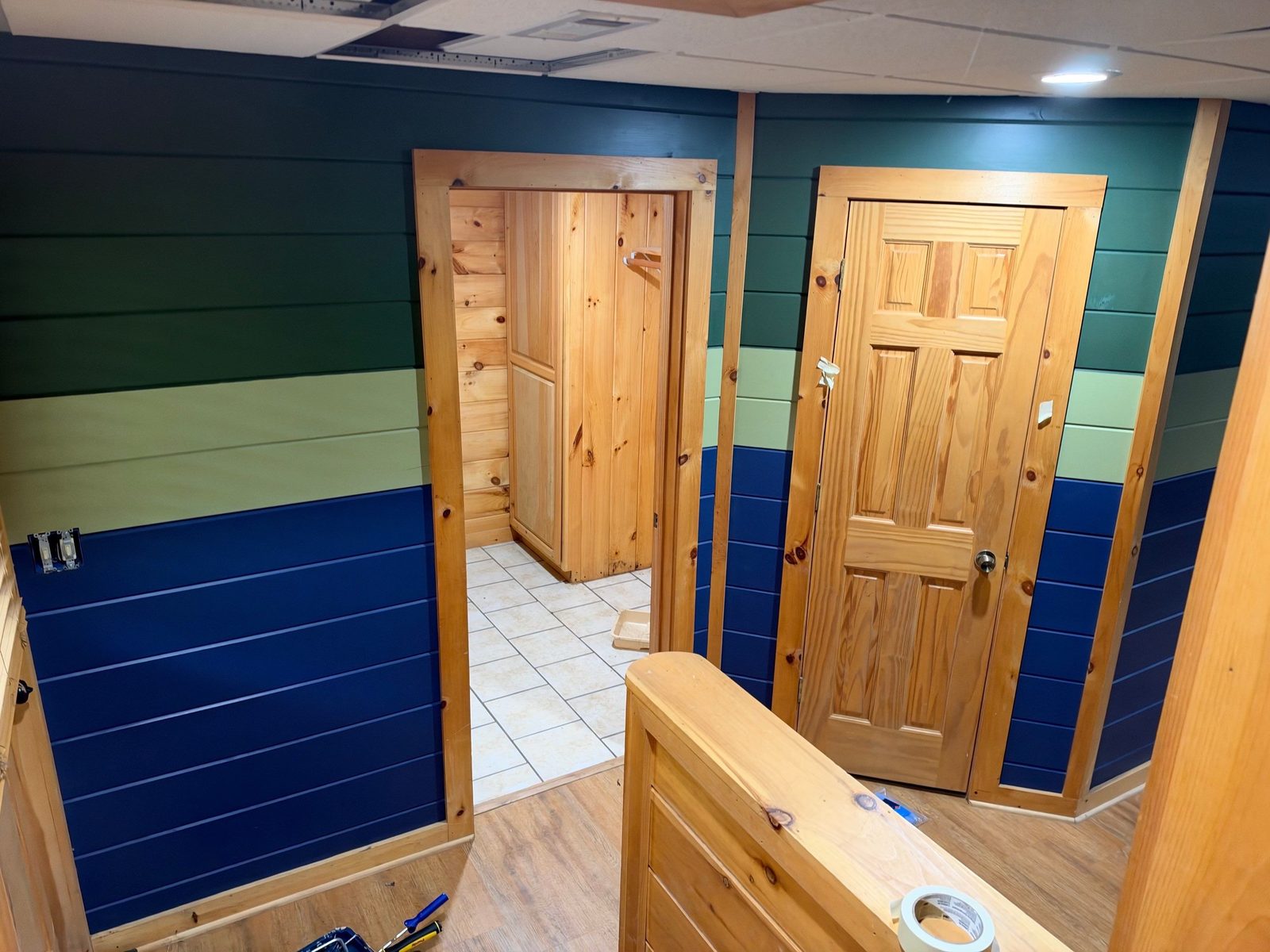 Basement hallway in a Blue Ridge cabin with striped green, sage and navy shiplap and pine doors