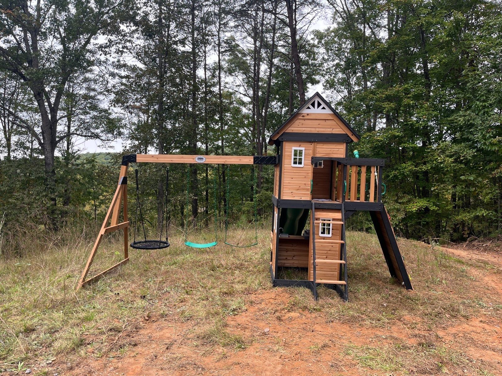 Swing set with a nest swing and two belt swings beside a wooden clubhouse at a Blue Ridge cabin