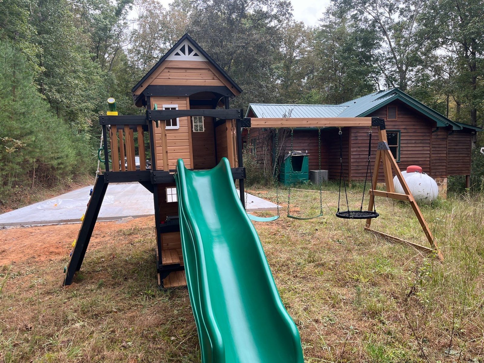 Wooden playset assembly in Blue Ridge, GA with a green wave slide, swings and covered clubhouse